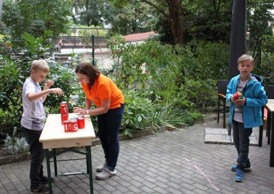 Frau Jenny Müller draußen auf dem Hof beim beim Dosenwerfen mit zwei Kindern.